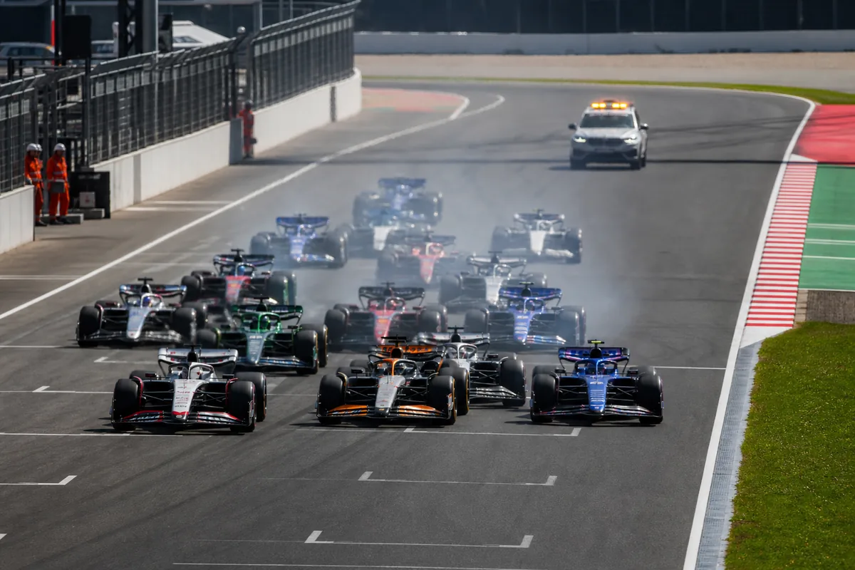 Formula-style race start with a neutral white medical support car following the field at a safe distance
